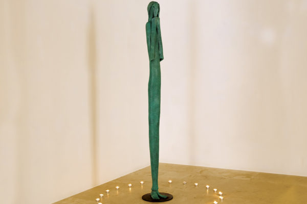 Escultura verde de bronce de una mujer de pie que se cubre la cara con las manos.